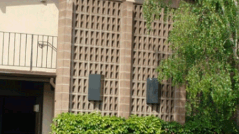 Facade of a multifamily property with a hedge and tree in front.