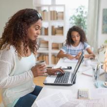 Woman working on a computer at her kitchen table.